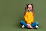 Fototapeta  - Full length photo of lovely kid dressed yellow sweatshirt denim pants sit near offer empty space isolated on khaki color background