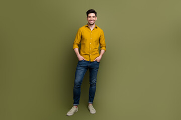 Wall Mural - Full length photo of attractive cheerful man wearing stylish clothes standing hands in pockets isolated on khaki color background