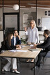 © fizkes - Serious senior boss woman talking to group of workers on meeting, explaining project plan, management strategy, standing at table, speaking to younger managers, raising arm for voting