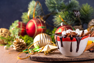 Wall Mural - Winter aromatic hot chocolate cup with Christmas background. Mug of dark hot cocoa drink with cinnamon, anise, spices and marshmallow, on cozy Christmas and New Year holiday decorated background 