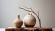 A rustic clay jug with natural textures, complemented by a handcrafted glass, both exhibited on a stand with organic forms against a clean white background.