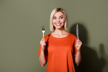 Wall Mural - Photo of adorable hungry young girl wear orange t shirt hold spoon knife delicious food in cafeteria isolated on khaki color background