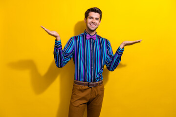 Poster - Portrait of pleasant guy dressed stylish shirt bow tie palms comparing products empty space isolated on vibrant yellow color background