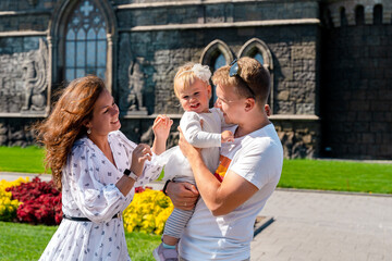 A young family mother father and child in a dress laughing against the background of a flower garden and a Garibaldi castle. Togliatti, Russia - 29 Aug 2023