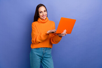 Poster - Photo of mature businesswoman in orange knitted trendy pullover holding macbook pro model for working isolated on purple color background