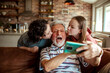 © Marko Geber - Grandfather taking a selfie on the smartphone with his grandchildren on the couch at home