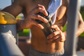 Wall Mural - One caucasian man young male athlete take a brake during outdoor training in the park outdoor gym hold supplement shaker in hand happy confident strong copy space