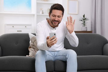 Wall Mural - Happy man greeting someone during video chat via smartphone at home