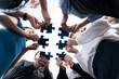 Leinwandbild Motiv Below view of diverse corporate officer workers collaborate in office connecting puzzle pieces as partnership and teamwork concept. Unity and synergy in business idea by merging jigsaw puzzle. Concord