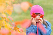 © Ermolaev Alexandr - Funny young girl with Downs syndrom holds autumn leaves lika eyeglasses. Empty space for text