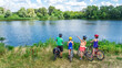 © Iuliia Sokolovska - Family on bikes cycling outdoors, active parents and kids on bicycles, aerial view of family with children relaxing near beautiful river from above, sport and fitness concept