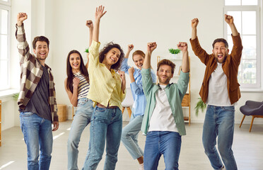 Wall Mural - Portrait of a group of excited happy young friends students or colleagues having fun hanging together at home. Men and women standing with raising hands up enjoying meeting and having a party.