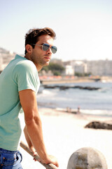 Poster - Thinking, fashion and man by ocean in city for summer holiday, vacation and weekend outdoors. Sunglasses, travel and confident person by sea in trendy clothes, style and casual outfit to relax