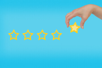 Woman's hand put the stars to complete five stars. Customer satisfaction concept. copy space and blue background. giving a five star rating. Service rating, satisfaction concept.