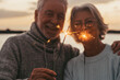 © Daniel - Couple of two old seniors holding sparklers lights at the evening at the beach together enjoying and having fun
