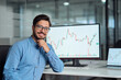© insta_photos - Young confident latin business man trader crypto investor broker looking at camera, portrait. Digital trade stock exchange charts on computer screen, investing in financial markets concept.