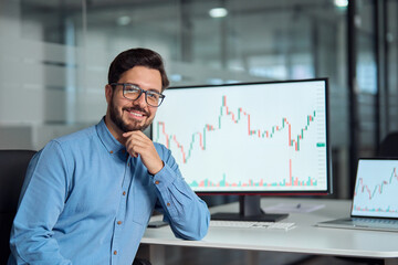 Young confident latin business man trader crypto investor broker looking at camera, portrait. Digital trade stock exchange charts on computer screen, investing in financial markets concept.