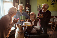Senior Man Holding A Birthday Cake With Friends At Home