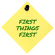 First Things First reminder green marker motivational text, important crucial business action concept, large isolated yellow post-it sticky adhesive note sticker, black pushpin thumbtack macro closeup