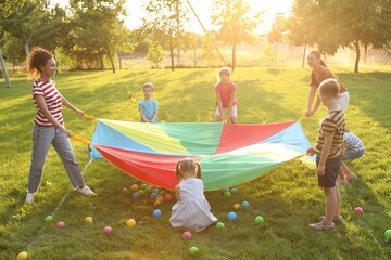 Wall Mural - Group of children and teachers playing with rainbow playground parachute on green grass. Summer camp activity