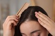 Woman with comb examining her hair and scalp on blurred background, closeup