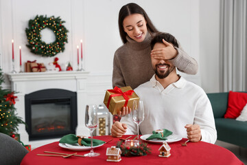 Poster - Happy woman surprising her boyfriend with Christmas gift at home