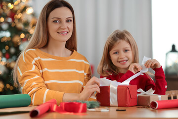 Wall Mural - Christmas presents wrapping. Mother and her little daughter decorating gift box with ribbon at home