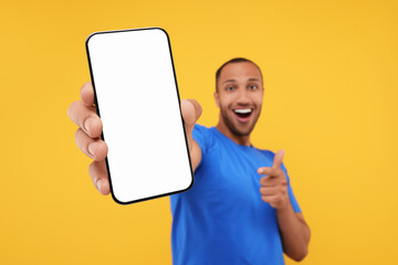 Sticker - Young man showing smartphone in hand and pointing at it on yellow background, selective focus. Mockup for design