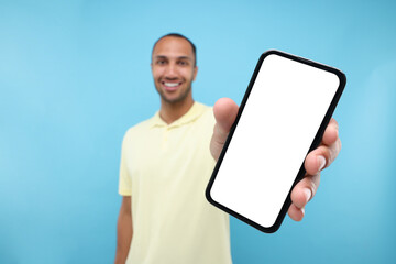 Wall Mural - Young man showing smartphone in hand on light blue background, selective focus. Mockup for design