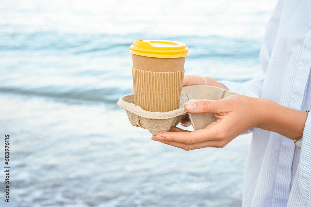 Woman holding paper coffee cup by the sea