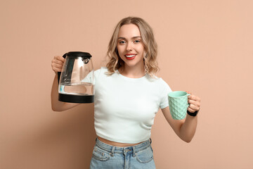 Poster - Beautiful young woman with modern electric kettle and cup on beige background