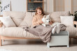© Pixel-Shot - Young woman with blanket and Samoyed dog on sofa warming near radiator at home