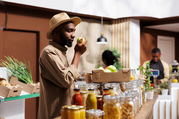 Black man admiring fresh fruits and embracing organic choices, prioritizing health and sustainability. Inhaling natural scents of green apples is an African American male customer with a hat.