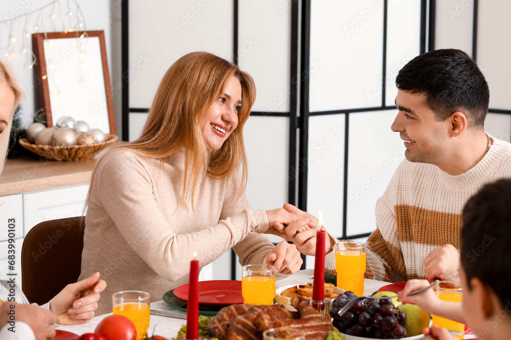 Happy young couple having Christmas dinner with their family at table in kitchen