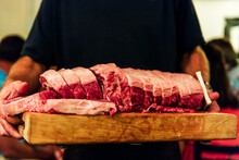 A Man Holds A Brown Butcher Block With Cuts Of Raw Ribeye Steak 