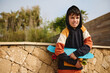 Multi ethnic teen boy skateboarder holding skateboard, looking at camera, standing against a stone wall background