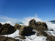 Tosende Welle schlägt gegen Felsen in der Brandung im Meer mit blauem Himmel im Hintergrund