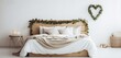 A Scandinavian-style bedroom with a wooden bed frame and white bedding. The bed is accented with a heart-shaped wreath made of eucalyptus leaves.