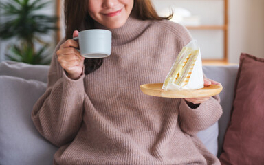 Wall Mural - Closeup image of a woman holding coffee cup and sandwich at home
