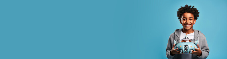 African-American boy look straight into the camera with robot in hands on blue studio background. Electric toys learning robots at robotics horizontal studio plain banner copy paste space for text
