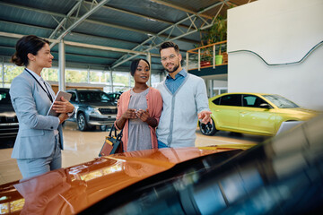 Wall Mural - Young multiracial couple looking for new car in showroom.