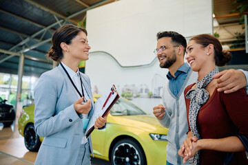 Wall Mural - Happy saleswoman talks to young couple who is buying new car in showroom.