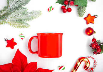 Blank red coffee mug mock up, fir tree branch, holly berries, poinsettia, candy cane and toys. Christmas New Year holiday season concept