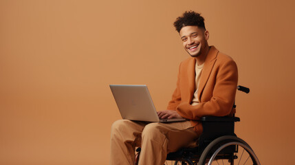 A young man in a wheelchair works on a laptop on a beige background