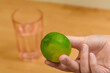 Zielona limonka trzymana w dłoni, w tle szklanka z wodą