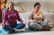 Happy african mother and adult daughter doing yoga meditiation at home during winter time