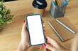 Female hands holding smartphone with mockup of blank screen on desk in office.