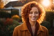 © kapros76 - Smiling young curly redhead attractive mature woman posing at a beautiful garden looking at the camera during late autumn sunset with a sun flares in the background, surrounded by friends and relative