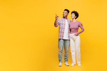 Wall Mural - Full body young couple two friends family man woman of African American ethnicity wears casual clothes together point index finger aside on area husband hug wife isolated on plain yellow background.