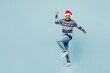 Full body young man wear sweater Santa hat posing do winner gesture celebrate clench fists say yes isolated on plain pastel blue background. Happy New Year 2024 celebration Christmas holiday concept.